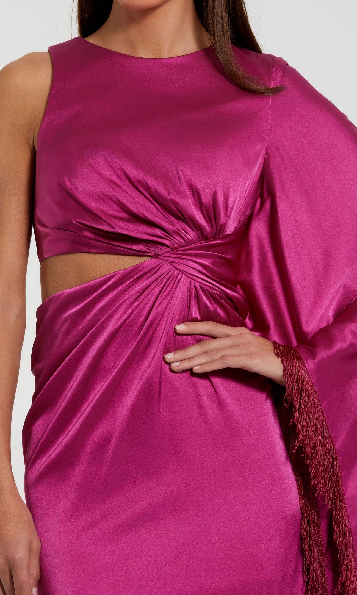 A woman showcasing the Long Formal Dress: Mac Duggal 49898, featuring shiny magenta charmeuse fabric, a sophisticated side cutout, gathered waist detailing, and an asymmetric sleeve adorned with fringe—capturing the elegant essence of this formal evening gown.